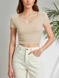 Dettaglio del crop top a coste beige con scollo a U e pantaloni bianchi a vita alta