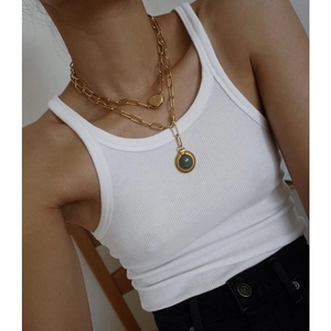 Detail of layered gold necklaces featuring a heart charm and turquoise pendant on cotton tank