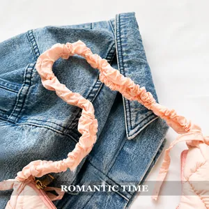 Detail of pink quilted shoulder bag featuring soft ruched handle on denim jacket background
