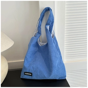 Détail du sac cabas en velours côtelé bleu montrant l'étiquette logo et la texture