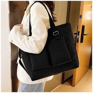 Close-up of black canvas tote bag featuring dual front pockets and durable shoulder strap