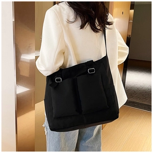 Detail view of large black canvas crossbody bag with two front flap pockets and metal buckles