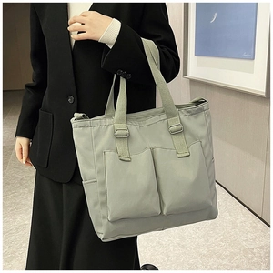 Close-up of light green canvas tote bag with dual front pockets and adjustable strap