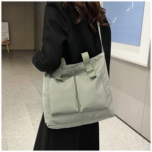 Model wearing a large light green canvas tote bag with dual front pockets in a modern hallway