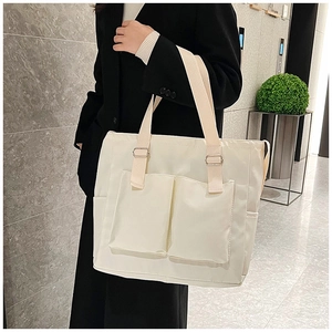 Detail of cream canvas tote bag showing two front utility pockets and adjustable straps