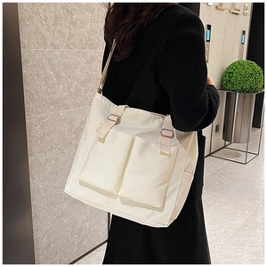 Detailed side view of off-white nylon tote bag with front pockets on model's shoulder