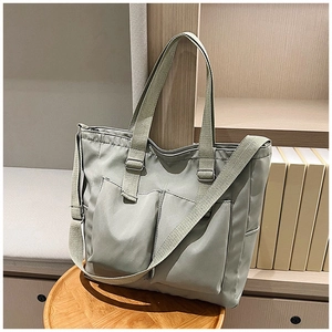 Detail of grey-green nylon tote bag with front pockets on a wooden tray with books
