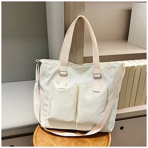 Detail of minimalist beige canvas tote bag with dual front pockets on a wooden stool