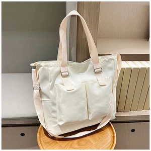 Detail of off-white large capacity tote bag with front pockets on a wooden stool