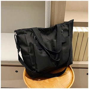 Detail of black canvas tote bag with dual front pockets on a wooden stool
