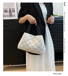 Détail du sac matelassé argenté avec larges anses en tissu noir et finition métallisée
