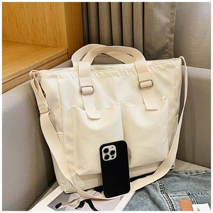 Detailed view of cream canvas tote bag with adjustable strap next to a smartphone for scale
