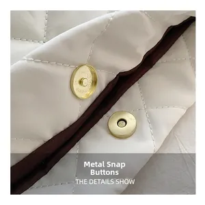 Detail view of gold metal snap button on quilted white fabric with brown trim