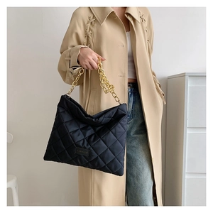 Detail of black quilted tote bag featuring golden chain straps and embroidery details