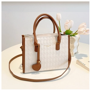 Detail of white quilted handbag with brown trim and heart charm accessory
