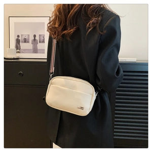 Close-up of cream lychee texture crossbody bag with striped wide strap and metal logo