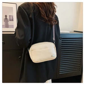 Detail of beige lychee leather camera bag with striped wide shoulder strap on model