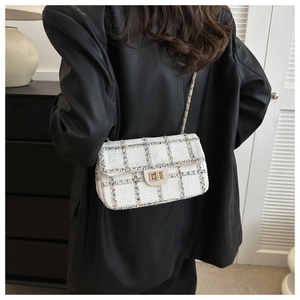 Detail van tweed crossbodytas met gouden slot en kettingriem op een zwart leren jasje