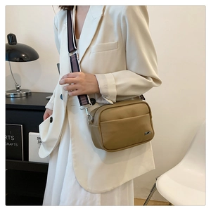 Detail of tan lychee pattern cross-body bag with adjustable striped wide shoulder strap