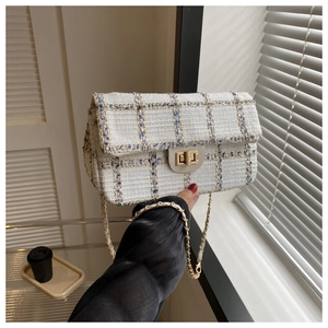 Detailopname van de getextureerde tweed stof en goudkleurige kettingriem van de tas