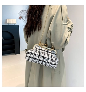 Detail van een zwart-witte tweed tas met gouden metalen sluiting en een fijne kettingriem