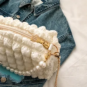 Detail of white bubble pleated fabric handbag with smooth gold zipper and pearl chain