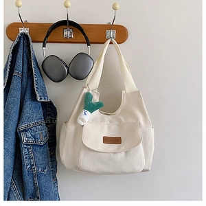 Détail d'un cabas en toile beige avec poche frontale et joli pendentif en peluche vert