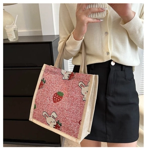Mirror selfie showing a red woven tote bag with strawberry and white rabbit patterns
