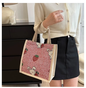 Detailansicht der gewebten Handtasche mit Erdbeer-Hasen-Muster und cremefarbenen Henkeln