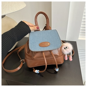 Detail of blue denim patchwork backpack with brown leather trim and pink plush charm