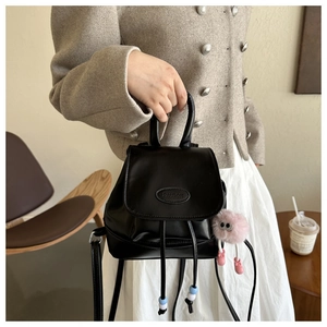Detalle de una mini mochila negra con cierre de cordón y adorable amuleto de peluche rosa