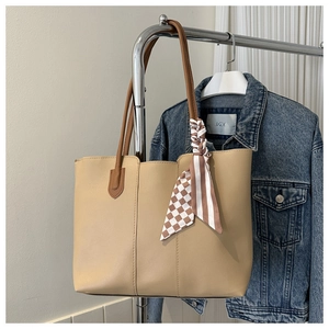 Detail der cremefarbenen Tragetasche mit braunem Griff und dekorativem Seidenschal-Accessoire