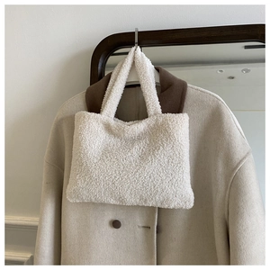 Close-up of cream fuzzy plush tote bag hanging with stylish wool coat background