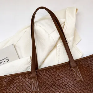 Detail view of the brown woven tote bag handle with reinforced cross stitching and texture