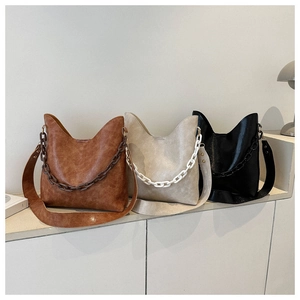 Tres bolsos tipo cubo de cuero en marrón, beige y negro con asa ancha y cadena decorativa