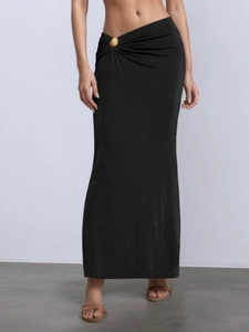Detail view of black asymmetric maxi skirt featuring a gold shell metallic waist ornament