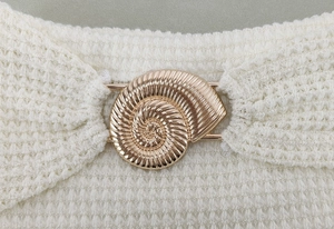 Détail du tissu gaufré blanc avec un grand accessoire décoratif en métal doré en forme de conque