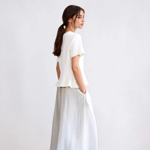 Detailed view of white short-sleeved top with ruffle hem and light grey maxi skirt
