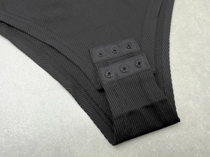 Detail of the black ribbed bodysuit featuring a secure triple snap button crotch closure