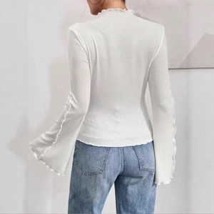 Close-up of white knitted top showing elegant lettuce trim on the back and flared sleeves
