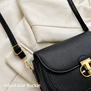 Close-up of golden adjustment buckle and rotary lock on black grain leather crossbody bag