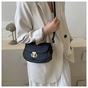 Detail of a black textured saddle bag with a golden turn-lock worn over a beige blazer