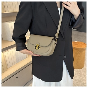 Close-up of khaki leather saddle bag with gold geometric buckle on elegant model