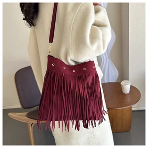 Detail of burgundy fringe tote bag with gold eyelets worn over an elegant white coat