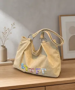 Detail of beige corduroy tote bag featuring STUFF embroidery and silver metal rings