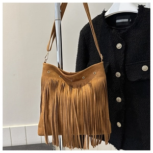 Detail of brown suede tassel bag with fringe and metal hardware on tweed jacket