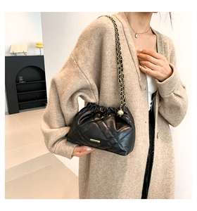 Detail of black quilted leather bucket bag with gold chain strap on beige knit cardigan