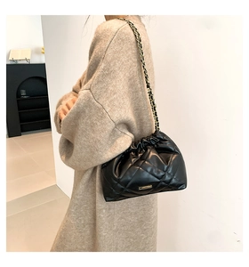 Detail of black quilted chain bag with gold metal hardware and woven leather strap