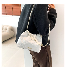 Detail of white quilted bucket bag with golden chain strap and drawstring closure