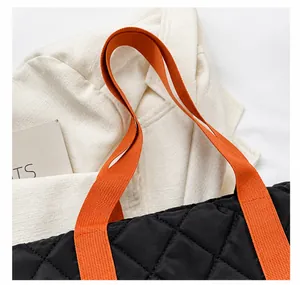 Detail einer schwarzen gesteppten Tragetasche mit leuchtend orangen Nylongriffen